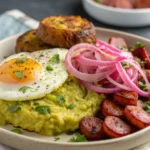 Mangu con tres golpes with fried egg, pickled onions, crispy salami, and tostones on a plate.