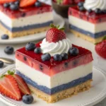 Layered berry jello lasagna dessert with whipped cream, strawberries, and blueberries.