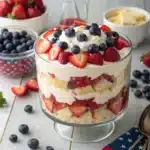 Layered 4th of July trifle with strawberries, blueberries, cake, and whipped topping in a glass pedestal bowl