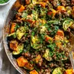 Close-up of ground beef, sweet potato, and zucchini skillet with fresh herbs.