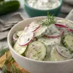 Creamy cucumber salad topped with fresh dill in a white speckled bowl