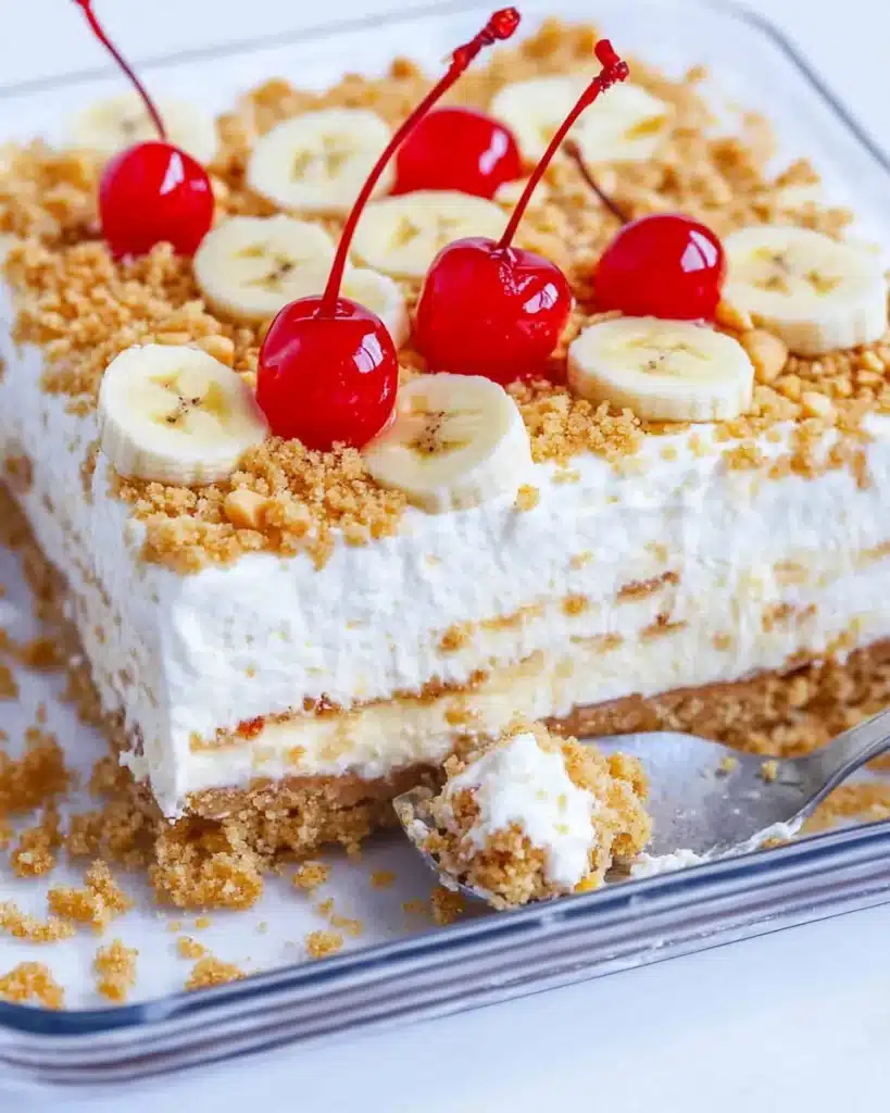 Close-up of a no bake banana split cake slice with cherries and peanuts.