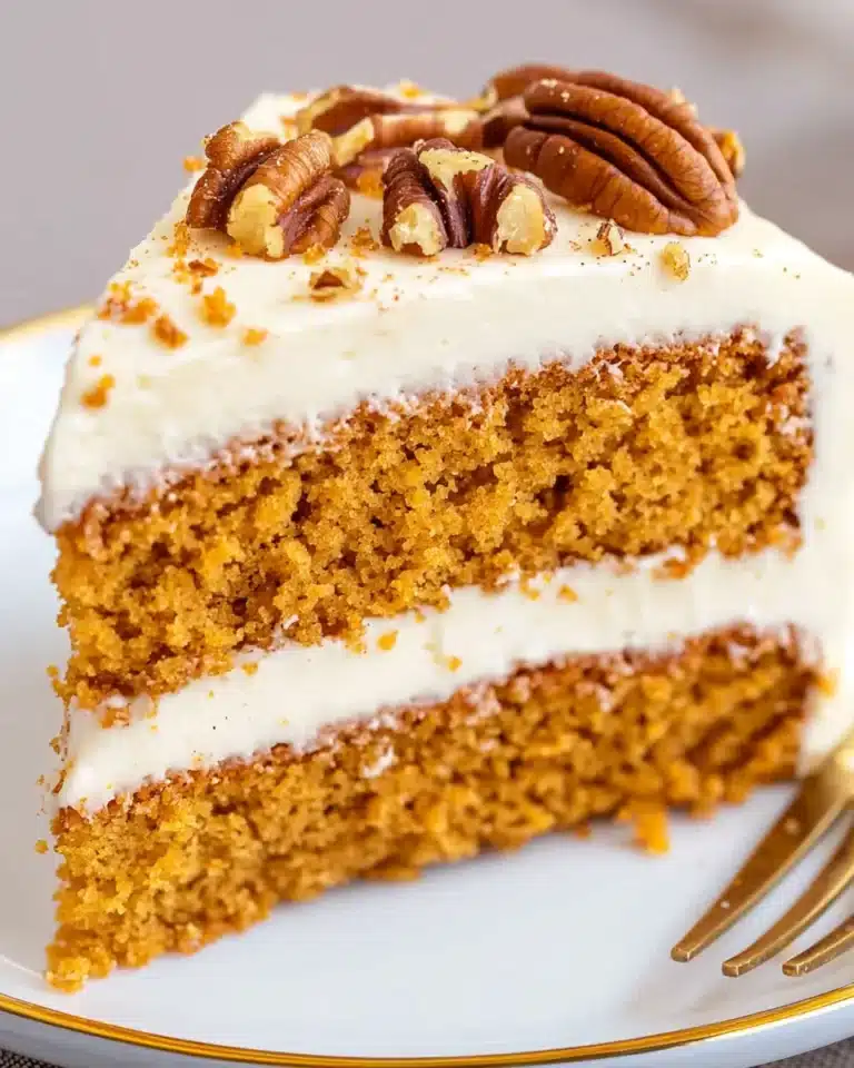 Slice of pumpkin spice cake with cream cheese frosting and pecan garnish