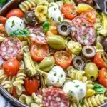 Antipasto pasta salad with salami, mozzarella, olives, cherry tomatoes, and artichokes.