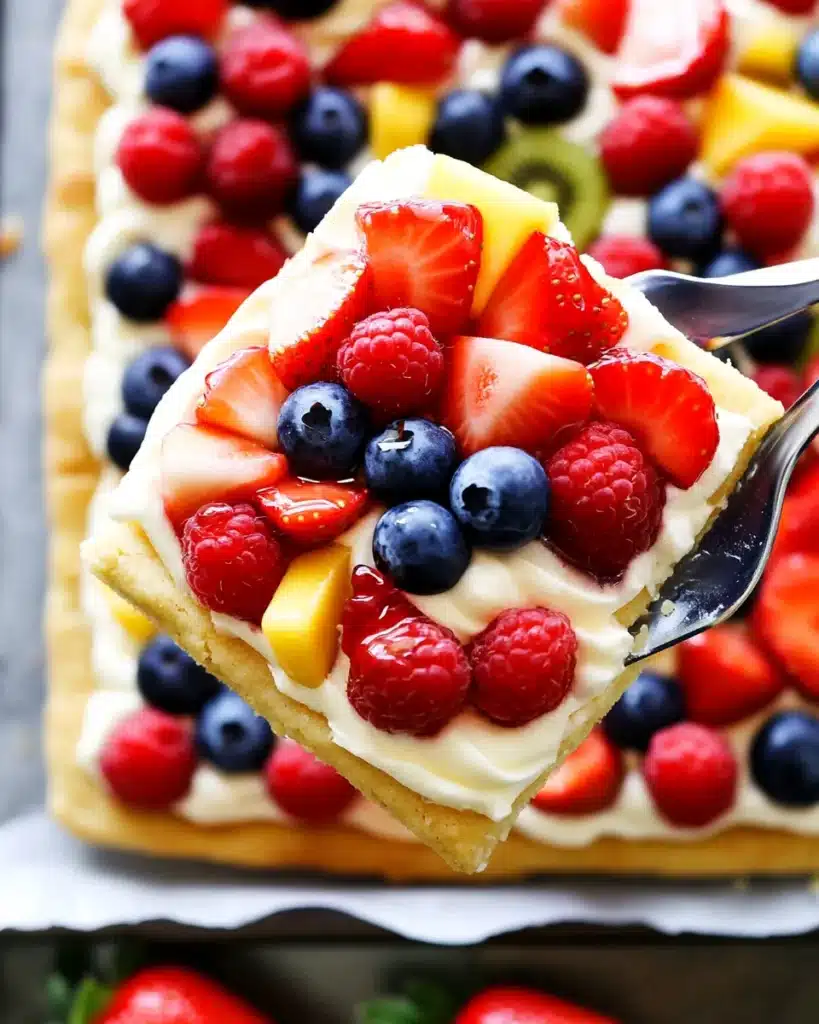 Close-up of fruit pizza slice with berries, kiwi, and mango being lifted from tray.
