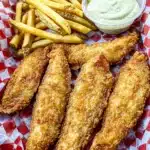 Golden fried catfish fillets with fries and dipping sauce on red checkered tray