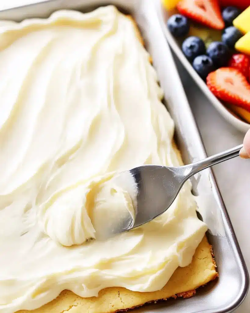 Cream cheese frosting being spread on baked sugar cookie crust for fruit pizza.