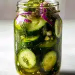Jar of sliced cucumber refrigerator pickles with dill, garlic, mustard seeds, and red onion.