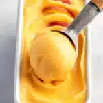 Scoop of no-churn peach sorbet in metal pan with peach slices