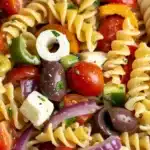 Close-up of rotini pasta salad with cherry tomatoes, olives, red onions, bell peppers, and mozzarella.