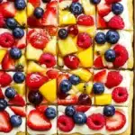 Colorful sliced fruit pizza with strawberries, blueberries, raspberries, and mango on sugar cookie crust.
