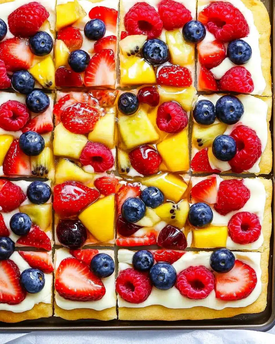 Colorful sliced fruit pizza with strawberries, blueberries, raspberries, and mango on sugar cookie crust.