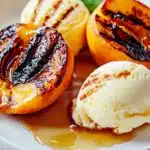 Grilled peaches served with scoops of vanilla ice cream and syrup drizzle.