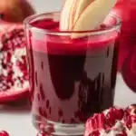 Fresh beetroot, apple, and pomegranate juice in a clear glass with apple slices garnish.