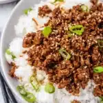 Close-up of ground beef and rice with sesame seeds and green onions.