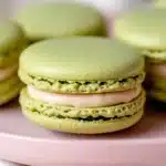 Light green pistachio macarons with creamy filling on pink plate