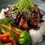Bourbon chicken over rice with broccoli and stir-fried vegetables.