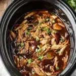 Crock Pot bourbon chicken topped with green onions in rich sauce