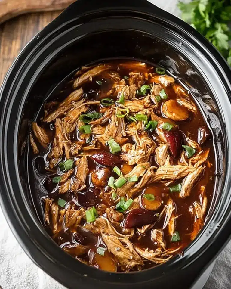 Crock Pot bourbon chicken topped with green onions in rich sauce