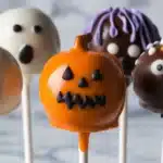 Colorful Halloween cake pops shaped like pumpkins, ghosts, and monsters on white sticks