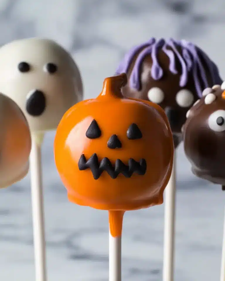 Colorful Halloween cake pops shaped like pumpkins, ghosts, and monsters on white sticks