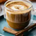 Glass mug of pumpkin coffee with cinnamon sticks on green plate