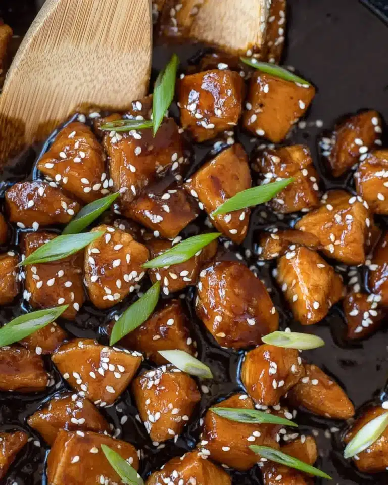 Glazed bourbon chicken with sesame seeds and green onions in skillet.
