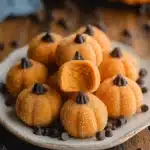Mini pumpkin-shaped cheesecake truffles with sugar coating and chocolate chip stems.