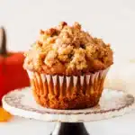 Single apple pumpkin muffin with golden cinnamon streusel on cake stand.