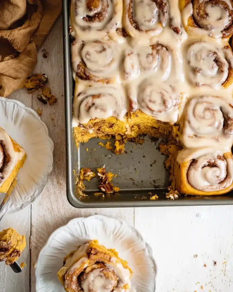 Pumpkin cinnamon rolls in baking pan with cream maple icing
