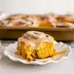 Soft pumpkin cinnamon roll with maple coffee icing on a white plate