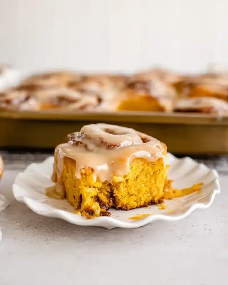 Soft pumpkin cinnamon roll with maple coffee icing on a white plate