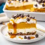 Slice of pumpkin lush dessert with graham crust, whipped cream, caramel, and chocolate chips