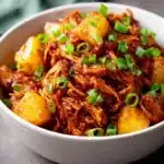 Shredded BBQ chicken with pineapple and green onions in a white bowl
