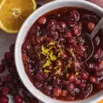 Fresh cranberry orange sauce in white bowl with zest garnish