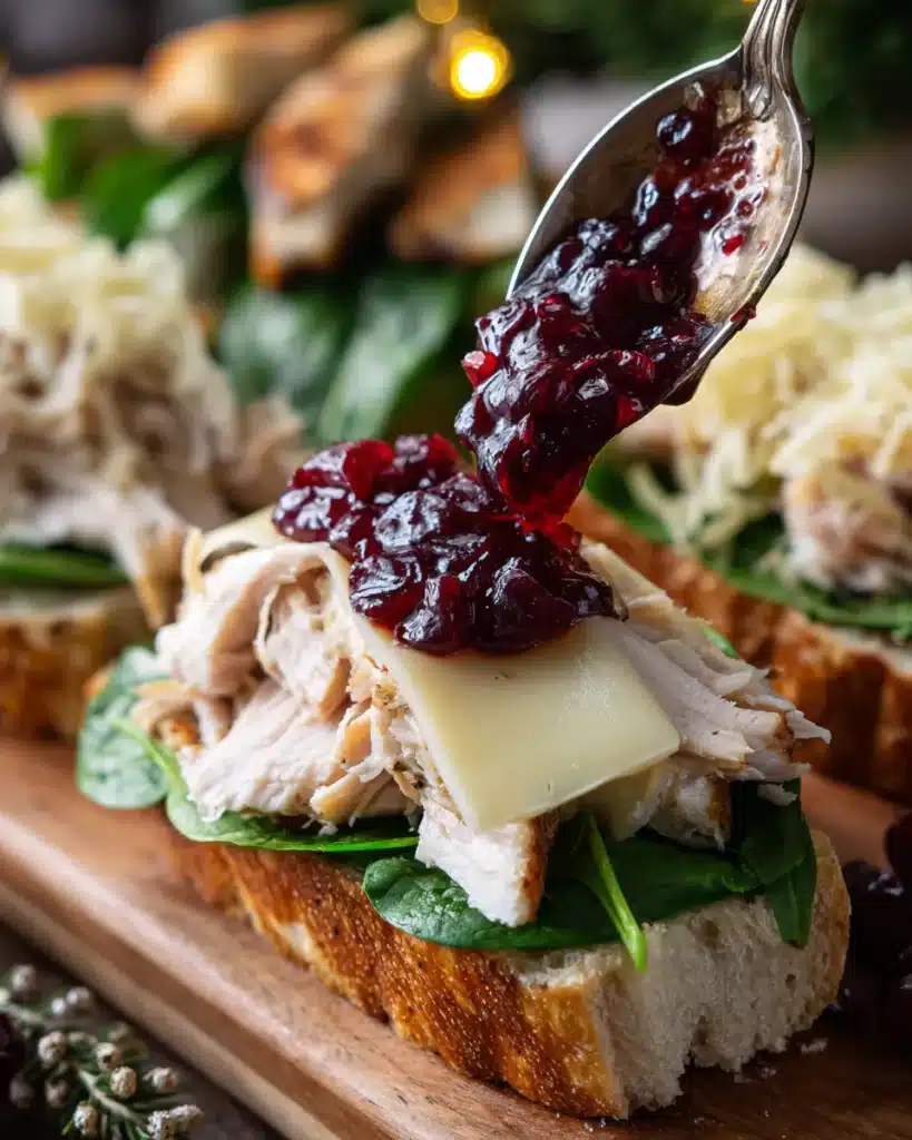 Spoon adding cranberry sauce to open-faced turkey sandwich with spinach and cheese