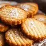 Golden French salted butter cookies topped with flaky sea salt on a silver plate