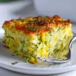 Golden zucchini cornbread casserole slice with corn and cheese on white plate