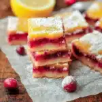 Stack of cranberry lemon bars with powdered sugar on parchment paper